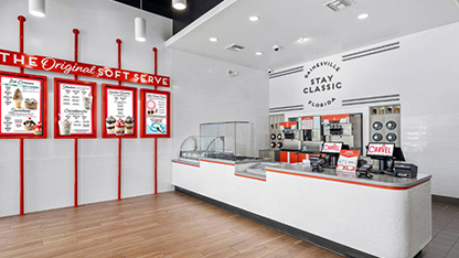 The store is spacious and well-lit, with a clean and modern aesthetic. There are multiple counters, each with menu boards featuring various food options. The counters have glass fronts, allowing customers to view the offerings inside. The walls are decorated with red and white stripes, adding a pop of color to the interior design. The lighting is bright, creating a welcoming atmosphere for customers.