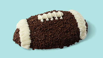 Image features cookie designed to resemble a football with white and brown trim. Cookie rests on blue surface.
